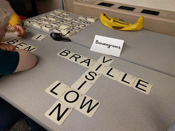 Tiles from the Bananagrams game spell out "BRAILLE" and "LOW VISION" in print and braille. 